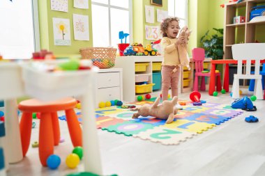 Adorable hispanic toddler holding doll standing at kindergarten