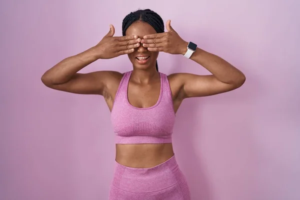 戴着辫子 身穿运动服 罩着粉色背景的非洲裔美国女人 双手含笑 笑逐颜开 盲目概念 — 图库照片