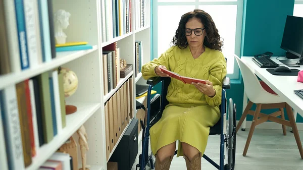 Orta Yaşlı Spanyol Kadın Öğretmen Kütüphanede Tekerlekli Sandalyede Kitap Okuyor — Stok fotoğraf