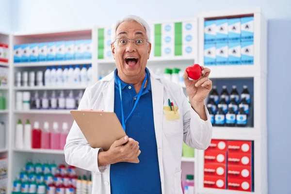 Мужчина Среднего Возраста Седыми Волосами Работающий Аптеке Держа Красное Сердце — стоковое фото