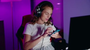 Kulaklıklı genç bir kadın akıllı telefonuyla evde müzik dinliyor.