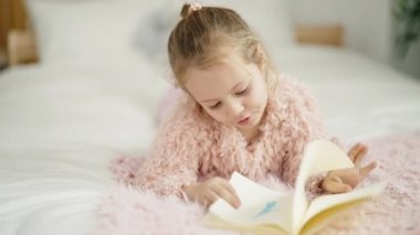 Adorable blonde girl reading book lying on bed at bedroom
