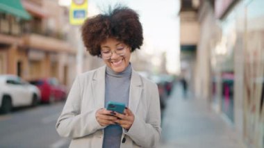 Afro-Amerikalı kadın sokakta akıllı telefon kullanarak kendine güveniyor.