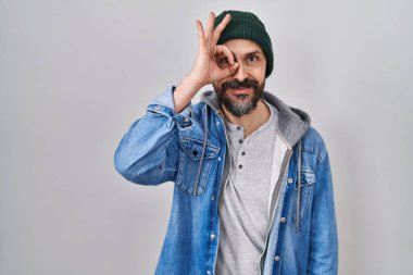 Dövmeli, yün şapkalı, el hareketleriyle gülümseyen, mutlu yüzüyle parmaklarının arasından bakan İspanyol bir adam.. 