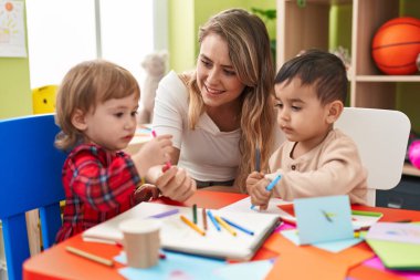 Teacher with boys sitting on table drawing on paper at kindergarten