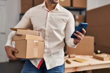 Genç İspanyol bir e-ticaret işçisi ofisteki akıllı telefon paketlerini kullanıyor.