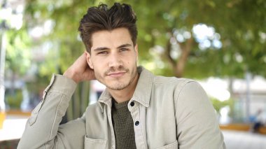 Young hispanic man standing with serious expression at park