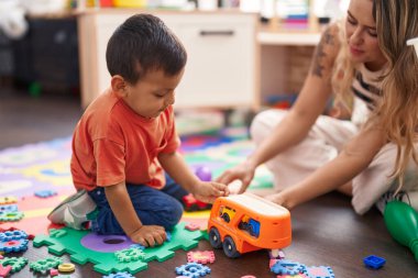Teacher and toddler playing with cars toy sitting on floor at kindergarten