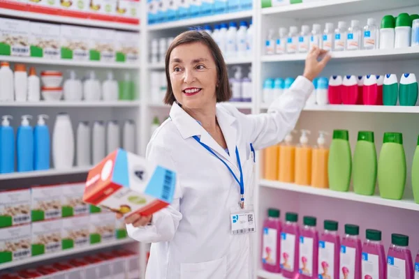 Kobieta Średnim Wieku Farmaceuta Uśmiechnięty Pewnie Trzymając Pakiet Witamin Aptece — Zdjęcie stockowe