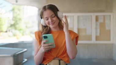 Üniversitede müzik dinleyip dans ederken kendinden emin gülümseyen genç bir kadın.