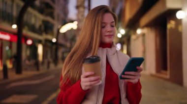 Genç sarışın kadın akıllı telefon kullanıyor. Sokakta kahve içiyor.