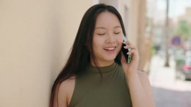Genç Çinli kadın gülümsüyor caddede akıllı telefondan konuşuyor.