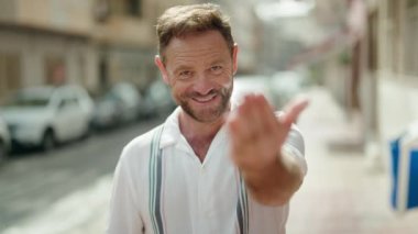 Middle age man smiling confident doing coming gesture with hand at street