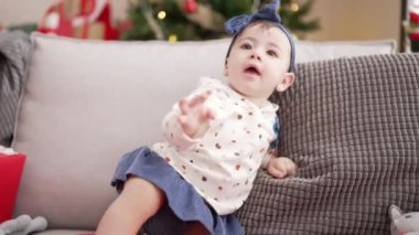 Evdeki noel ağacının yanındaki kanepede oturan sevimli bebek.