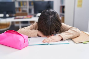 Adorable hispanic girl student stressed leaning on book at classroom