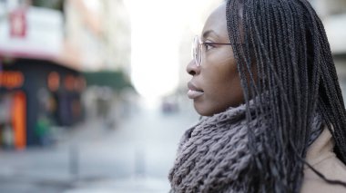 African woman standing from the side with serious expression wearing glasses at street