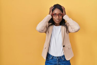 African young woman wearing glasses suffering from headache desperate and stressed because pain and migraine. hands on head. 