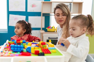 Teacher with girls playing with construction blocks sitting on table at kindergarten