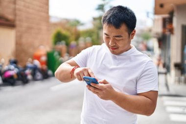 Young chinese man smiling confident using smartphone at street