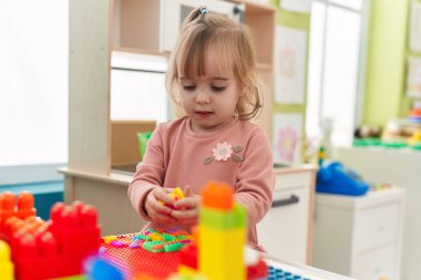 Adorable blonde girl playing with construction blocks standing at kindergarten