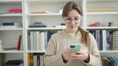 Young blonde woman student using smartphone at library university