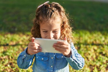 Sevimli sarışın çocuk, gülümsüyor. Parkta akıllı telefondan videolar izliyor.