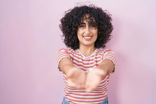 年轻的中东女人站在粉红的背景上 双手合十地微笑着 接受着或给予着手势 持有和保护 — 图库照片
