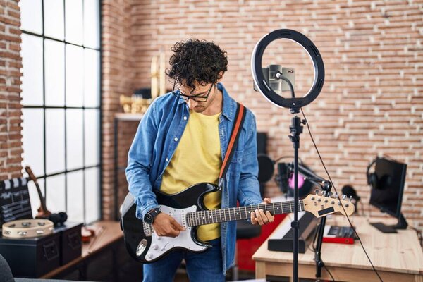Young hispanic man musician playing electrical guitar recording video at music studio