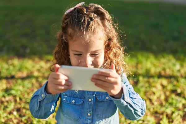 可爱的金发碧眼的幼儿在公园观看智能手机视频时充满自信地微笑 — 图库照片