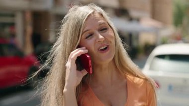 Genç sarışın kadın gülümsüyor. Kendine güveni tam. Akıllı telefondan konuşuyor.