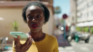 Afro-Amerikalı kadın gülümsüyor. Akıllı telefondan konuşuyor.
