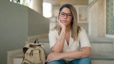 Young hispanic woman student smiling confident sitting on stairs at university