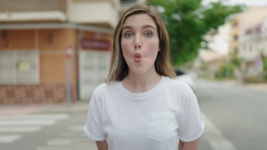 Sokakta duran ağzı olan genç bir kadın komik hareketler yapıyor.