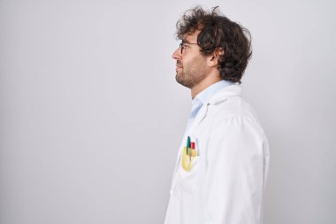 Hispanic young man wearing doctor uniform looking to side, relax profile pose with natural face with confident smile. 