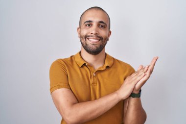 Hispanic man with beard standing over white background clapping and applauding happy and joyful, smiling proud hands together 