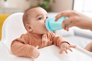 Tapılası İspanyol bebek evde şezlongda su içiyor.