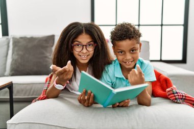 İki kardeş kanepede uzanıp kitap okuyorlar. Buraya el kol hareketi yaparak mutlu ve gülümseyen insanları davet ediyorlar. 