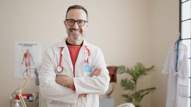 Middle age man doctor smiling confident standing with arms crossed gesture at clinic