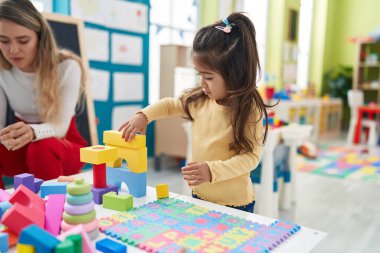 Teacher and toddler playing with geometry blocks sitting on table at kindergarten