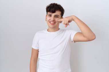 Young non binary man wearing casual white t shirt pointing with hand finger to face and nose, smiling cheerful. beauty concept 