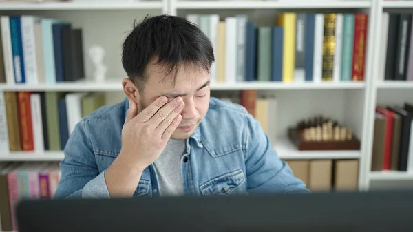Young chinese man student using computer stressed at library university