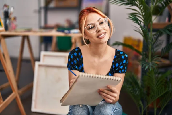年轻的高加索女艺术家微笑着在艺术工作室的笔记本上画出自信的图画 — 图库照片