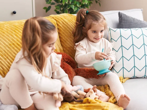 两个玩洋娃娃的孩子坐在家里的沙发上 — 图库照片