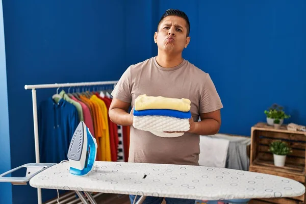 Hispanic young man holding folded laundry after ironing looking at the camera blowing a kiss being lovely and sexy. love expression.