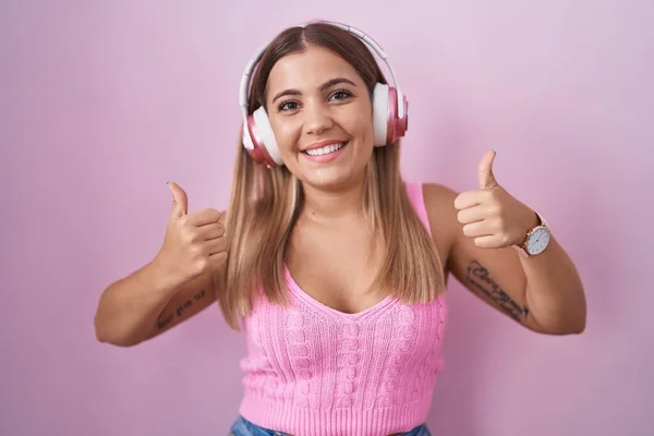 Young blonde woman listening to music using headphones success sign doing positive gesture with hand, thumbs up smiling and happy. cheerful expression and winner gesture.