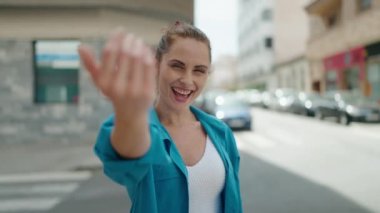 Young woman smiling confident doing coming gesture with finger at street