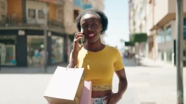 Afro-Amerikalı kadın akıllı telefondan konuşuyor. Elinde alışveriş torbaları var.