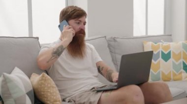 Genç kızıl saçlı adam dokunmatik ped kullanıyor. Evde akıllı telefondan konuşuyor.