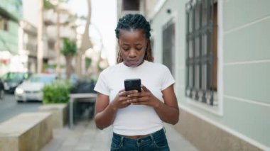 Afro-Amerikalı kadın sokakta akıllı telefon kullanarak kendine güveniyor.