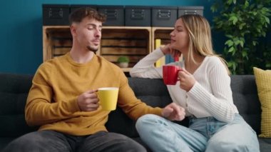 Young couple drinking coffee sitting on sofa at home